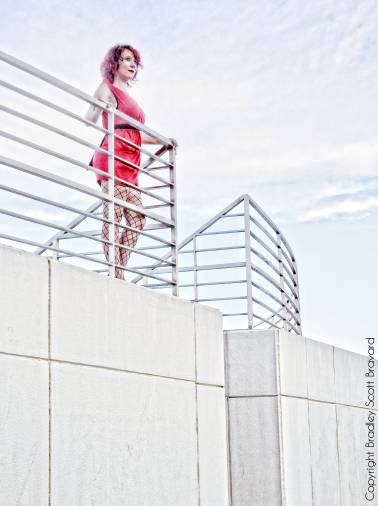 Woman in red dress standing on concrete ledge and looking into the distance