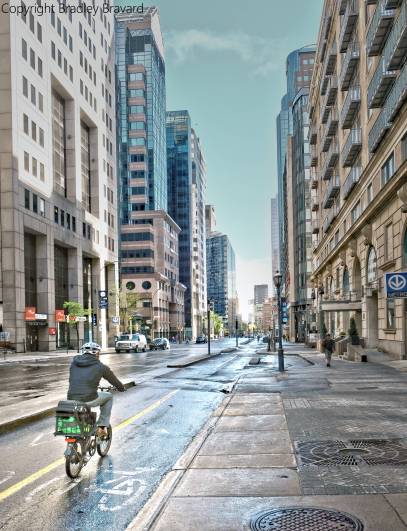 Photograph of bicyclist on city street surrounded by tall buildings in Montreal, Canada