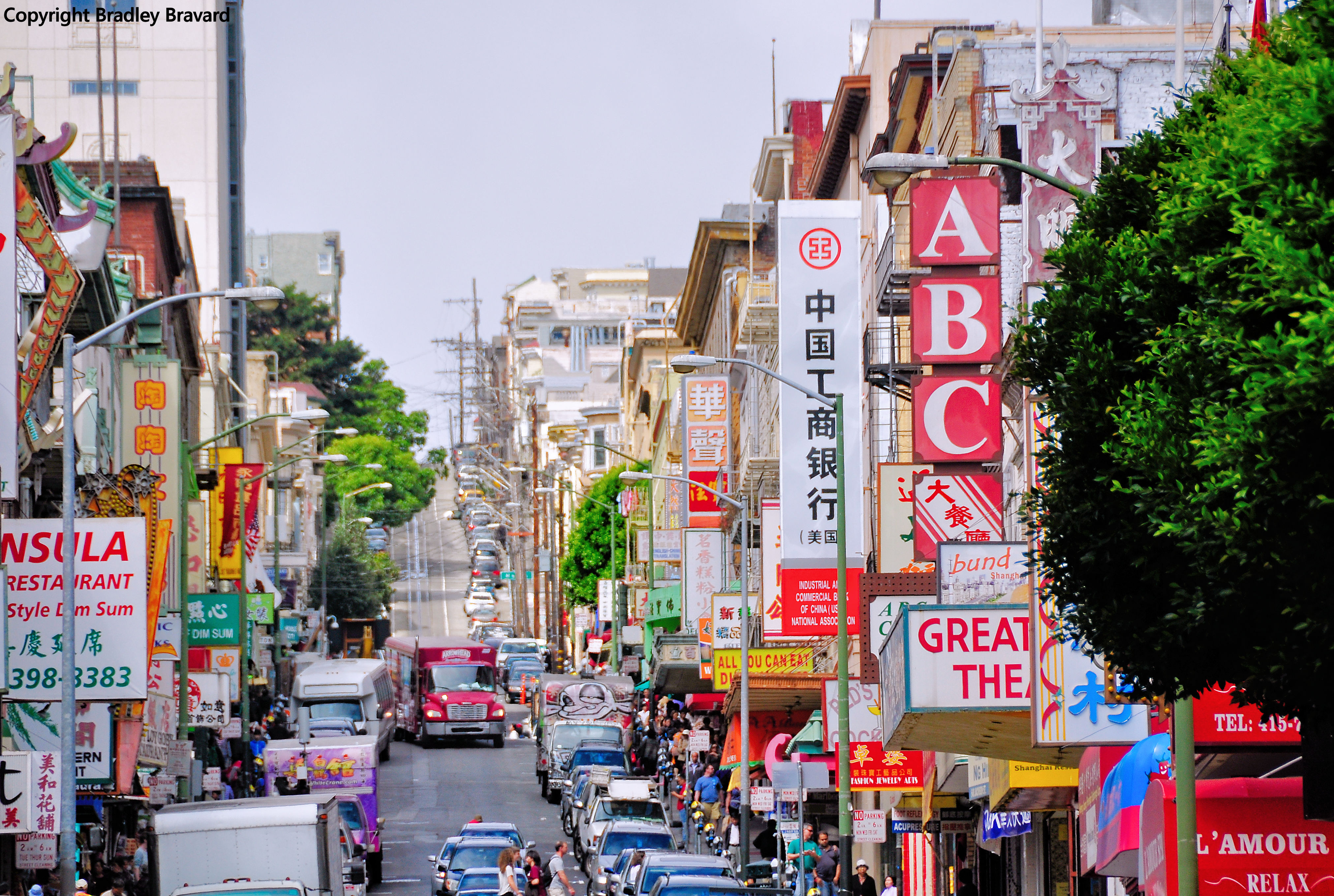 Color photo looking down a long street busy with traffic, signs, buildings, and pedestrians, in San Francisco