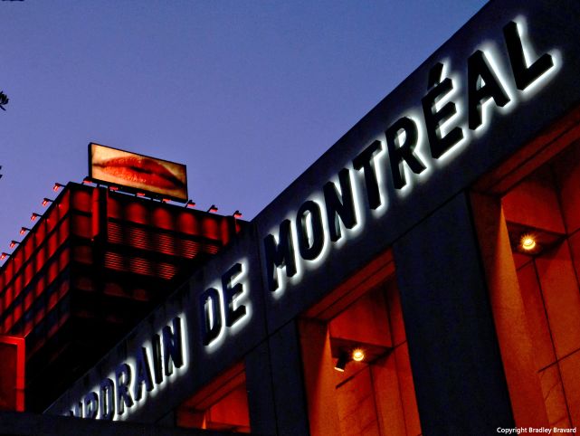 Night photo of sign for Museum of Contemporary Art in Montreal under a lighted billboard with an illustration of human lips