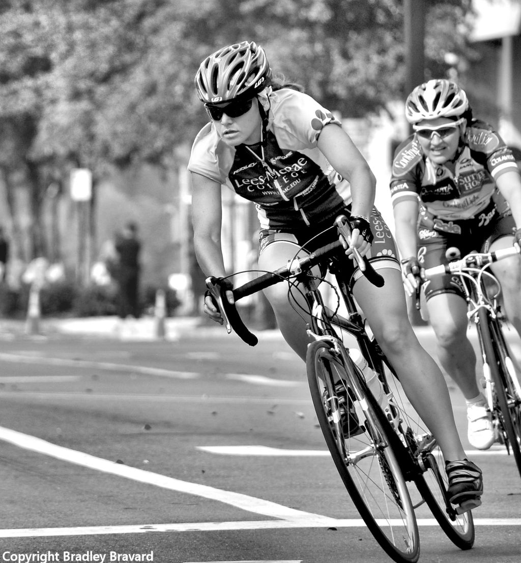 Black and white photo of two women on bicycles, wearing helmets and cycling gear