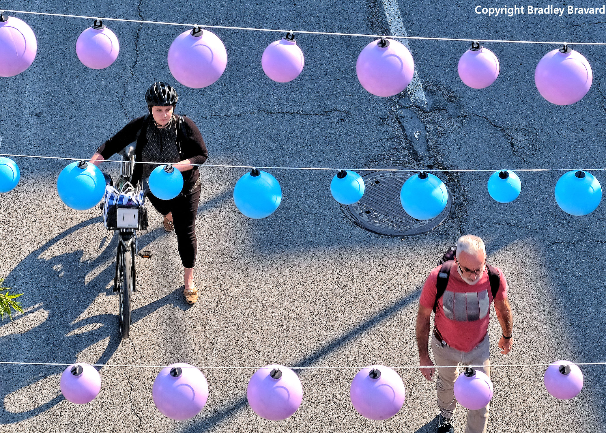 Photo of woman with bicycle and man walking in street viewed from overhead