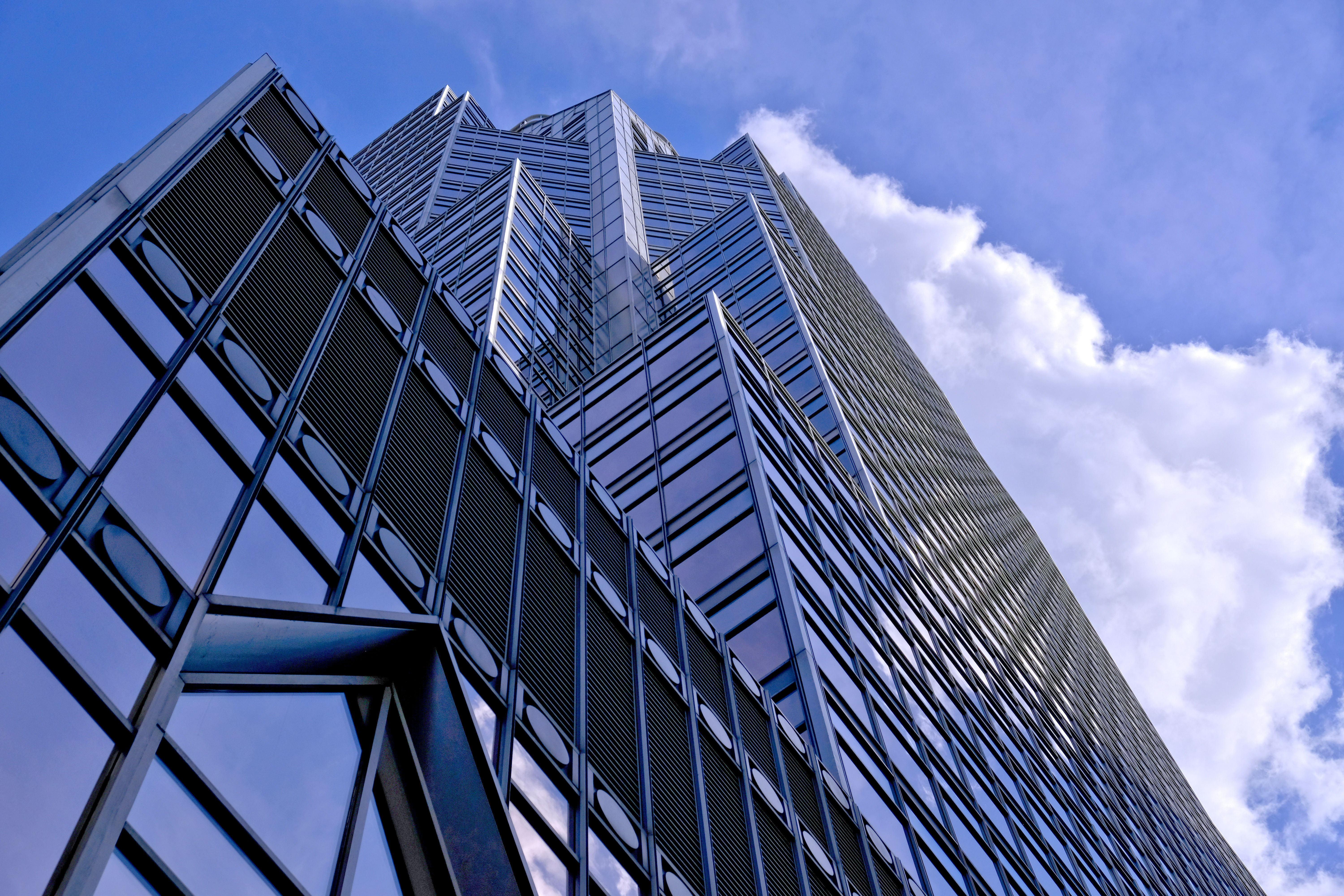 Photo at ground level looking up at glass skyscraper with partly cloudy sky in background