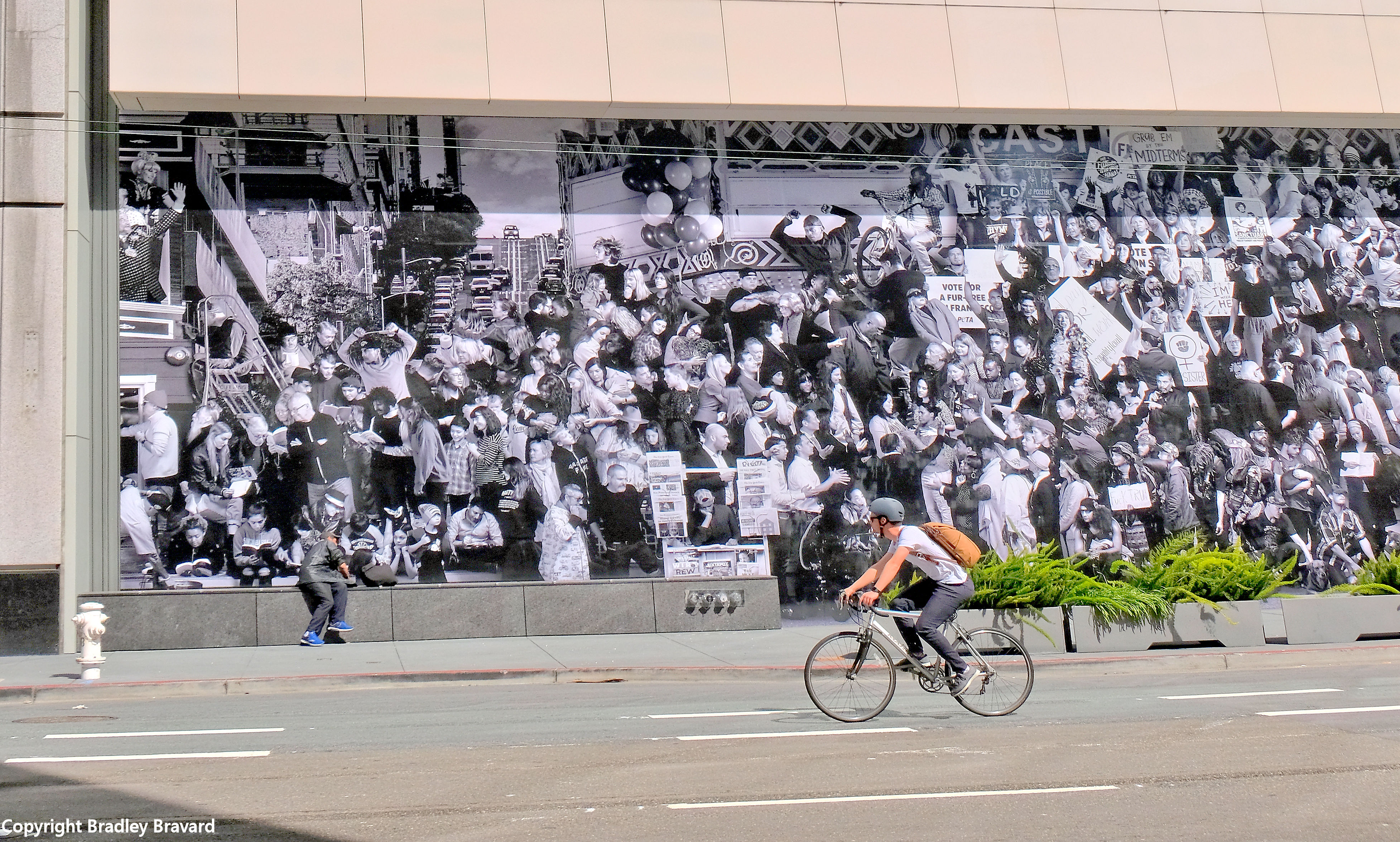 Man on bicycle in front of mural of crowd at San Francisco Museum of Modern Art